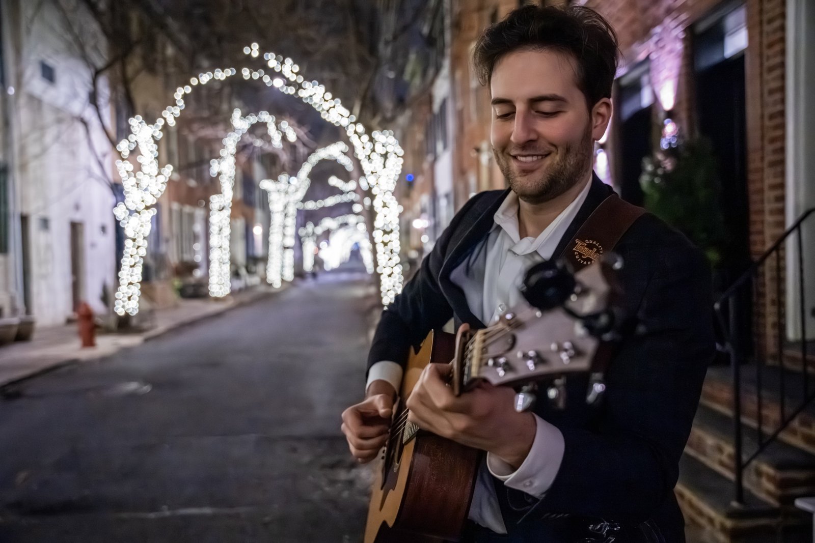 Lenny Miller playing guitar on a festively lit city street at night